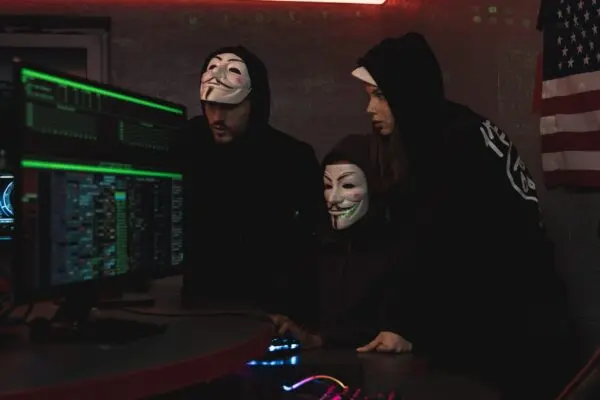 Three hackers in dark room using computers to breach crypto wallets and steal Bitcoin